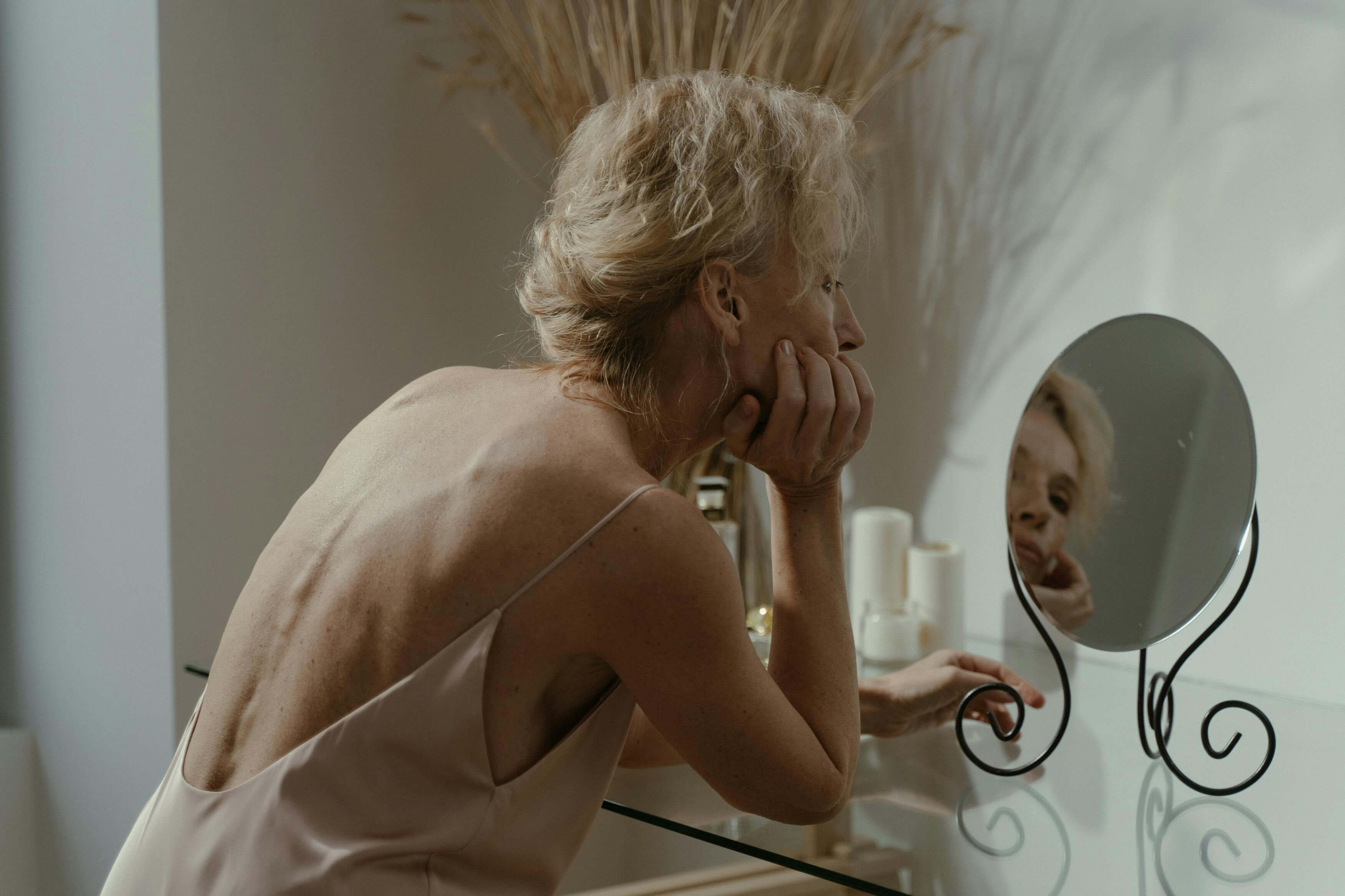 A woman at her vanity, looking at her own reflection — the moment every woman recognizes